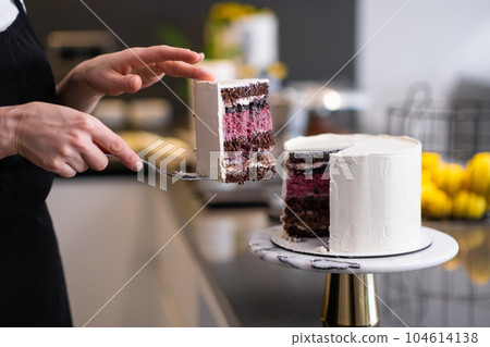 Self-made confectioner taking piece of homemade biscuit tiered shortcake with white mastic standing at kitchen table woman showing prepared custom pastry for wedding closeup Self-made confectioner taking piece of homemade biscuit tiered shortcake with white mastic standing at kitchen table woman showing prepared custom pastry for wedding closeup 104614138