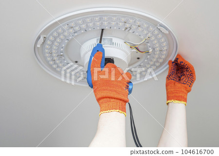 An electrician installs a chandelier on the ceiling.  104616700