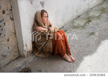 A girl in poor clothes sits on the ground A girl in poor clothes sits on the ground 104616966