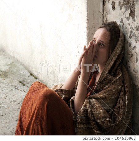 A girl in poor clothes sits on the ground A girl in poor clothes sits on the ground 104616968