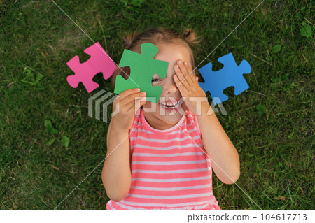 A ludicrous child is playing with puzzles while lying on the lawn grass. Children's toys for the development of logic and thinking A ludicrous child is playing with puzzles while lying on the lawn grass. Children's toys for the development of logic and thinking 104617713
