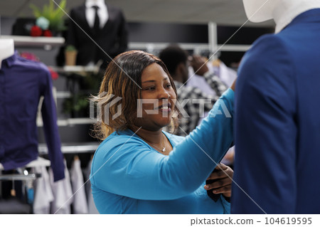 African american client checking blue suit, analyzing material in clothing store. Shopaholic woman looking at rack with new fashion collection, shopping for fashionable clothes in boutique 104619595