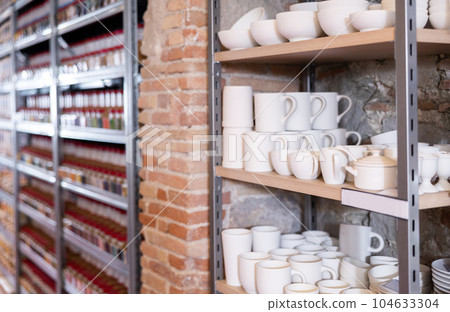 Various clay mugs and cups on racks in pottery shop 104633304