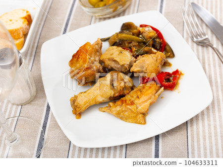 Roasted yummy chicken thigh and wings with fried eggplant and peppers served on the table with fresh olives, salt and cutlery 104633311