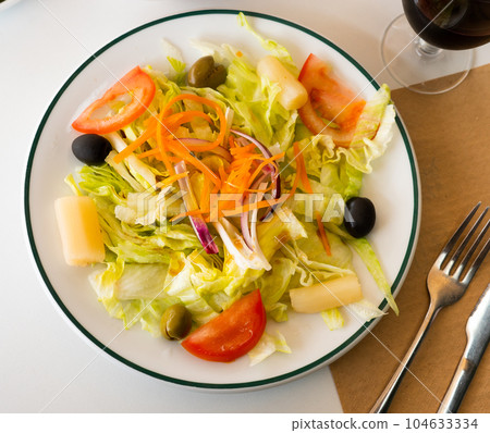Plate with vegetable salad with cabbage, lettuce, carrots, onions, tomatoes, olives 104633334