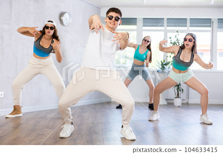Teenage girl practicing energetic dance movements with group of teens in choreography class Teenage girl practicing energetic dance movements with group of teens in choreography class 104633415