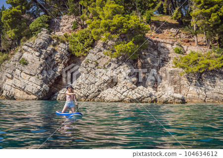Young women Having Fun Stand Up Paddling in blue water sea near st stefan island against the backdrop of Milocer Park in Montenegro. SUP 104634612