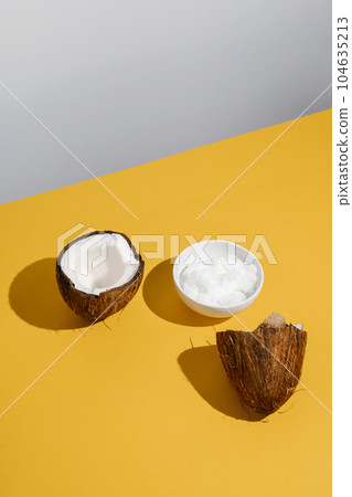 Two halves of coconut and coconut oil in a bowl. 104635213