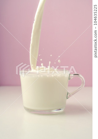 Milk is poured into a transparent cup on a purple background. Milk is poured into a transparent cup on a purple background. 104635225