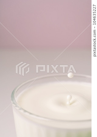 Milk drips into a transparent faceted glass. 104635227