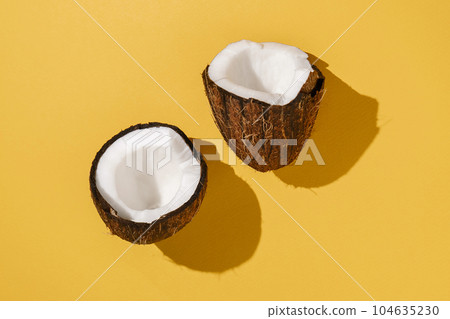 Two halves of coconut on a bright yellow background. 104635230