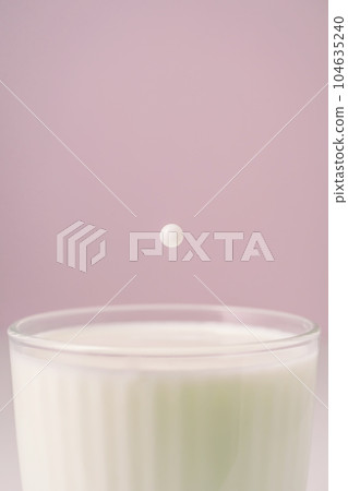 Milk drips into a transparent faceted glass. 104635240