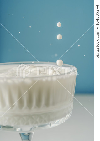 Milk pours into a beautiful crystal glass on a blue background and splashes around. 104635244