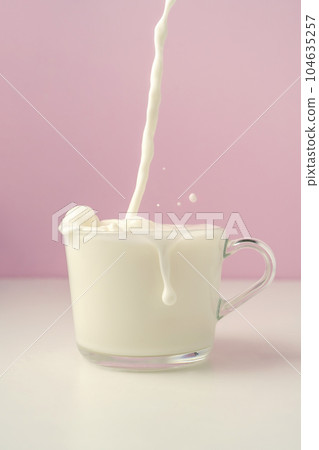 Milk is poured into a transparent cup on a purple background. 104635257