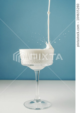 Milk pours into a beautiful crystal glass on a blue background and splashes around. 104635260
