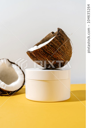 Two halves of coconut and a jar of cosmetics on a yellow and gray background. Two halves of coconut and a jar of cosmetics on a yellow and gray background. 104635264