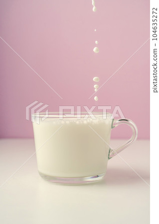 Milk is poured into a transparent cup on a purple background. 104635272