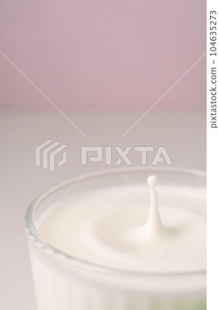 Milk drips into a transparent faceted glass. 104635273