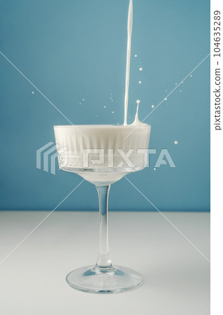 Milk pours into a beautiful crystal glass on a blue background and splashes around. 104635289