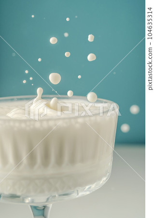 Milk pours into a beautiful crystal glass on a blue background and splashes around. 104635314