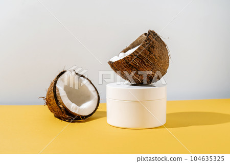 Two halves of coconut and a jar of cosmetics on a yellow and gray background. 104635325