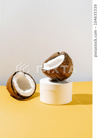 Two halves of coconut and a jar of cosmetics on a yellow and gray background. 104635339