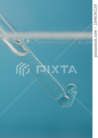 Pipette with cosmetic product in water with bubbles. 104636129