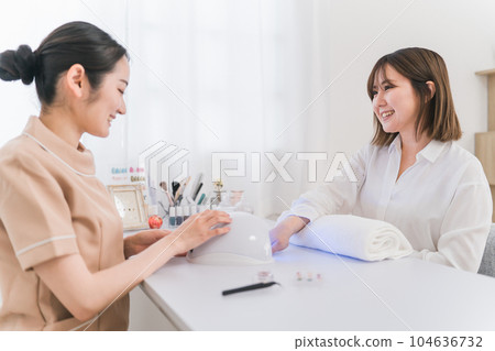 A woman doing nails at a nail salon and a manicurist (LED light/curing) 104636732