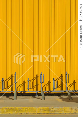 Vertical shot of bike parking near a bright yellow profiled metal wall, fence or warehouse idea, screen background or design articles 104639804