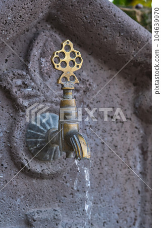Water flows from an old copper faucet, a vertical shot of a sink in a public place on the street of the old city in Turkey, travel time, an idea for a background 104639970