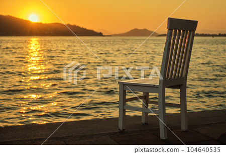 Sunset on the promenade by the sea, old chair in a cafe near the sea water on the Aegean coast, warm spring sunset, vacation time Sunset on the promenade by the sea, old chair in a cafe near the sea water on the Aegean coast, warm spring sunset, vacation time 104640535