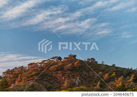 Scenic landscape of a hill against a sky of feather clouds in the red pink sunset light on the Aegean coast of Turkey, landscape or screensaver idea 104640675