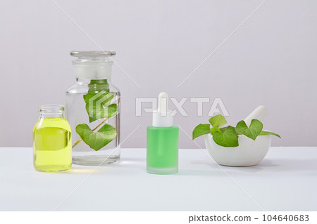 Front view of dropper bottle unlabeled decorated on white background. Lab glassware containing fish mint leaves and essence. Mockup scene for advertising cosmetic of natural extract.  104640683