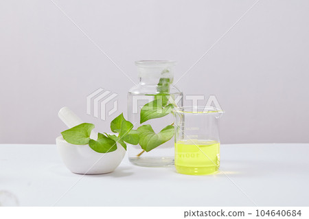 Minimalist background for fish extract cosmetic presentation with laboratory concept. Glassware containing yellow liquid and fresh fish mint leaves and pestle and mortar decorated on white background 104640684