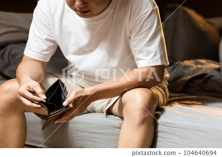 Stressed asian man having no money,holding empty wallet,Depressed male sitting in bed at night,financial trouble,bad economy,problems of economic recession,great depression,economic downturn concept 104640694