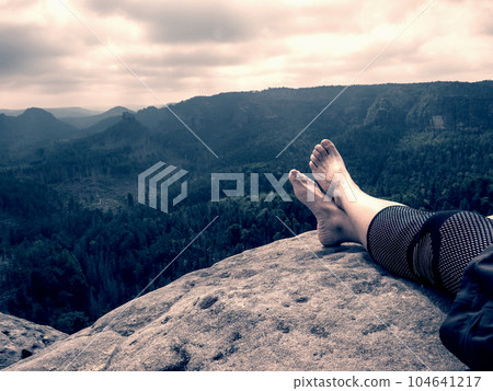 Crossed female barefoot legs of man relax on mountain summit. Hiker lay down and have a rest Crossed female barefoot legs of man relax on mountain summit. Hiker lay down and have a rest 104641217
