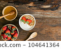 Strawberry yogurt in a wooden bowl with granola, honey, mint and fresh strawberry on wooden background. Health food concept 104641364