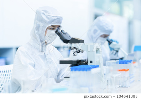A researcher conducting an experiment using a microscope in a clean room A researcher conducting an experiment using a microscope in a clean room 104641393