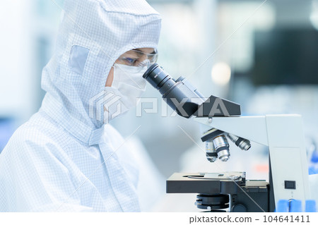 A researcher conducting an experiment using a microscope in a clean room 104641411