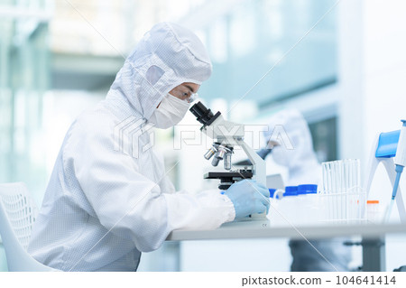 A researcher conducting an experiment using a microscope in a clean room A researcher conducting an experiment using a microscope in a clean room 104641414