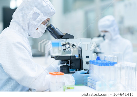 A researcher conducting an experiment using a microscope in a clean room A researcher conducting an experiment using a microscope in a clean room 104641415