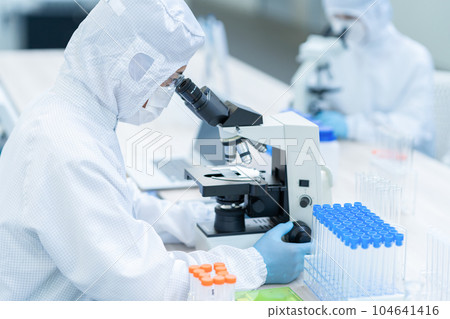 A researcher conducting an experiment using a microscope in a clean room A researcher conducting an experiment using a microscope in a clean room 104641416