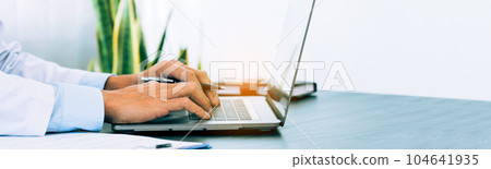 Doctor was sitting in the office working on a laptop computer. Doctor was sitting in the office working on a laptop computer. 104641935