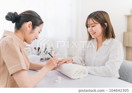 Manicurist and woman applying base coat at nail salon Manicurist and woman applying base coat at nail salon 104642305