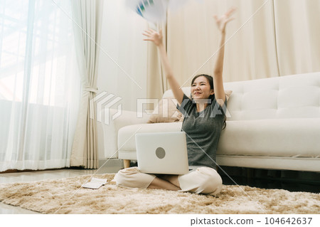 Asian woman throws papers in the living room as she finishes her work with her laptop on her lap. Asian woman throws papers in the living room as she finishes her work with her laptop on her lap. 104642637