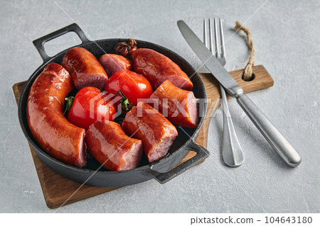 sliced fried pork sausage in a cast iron pan with tomatoes and c 104643180