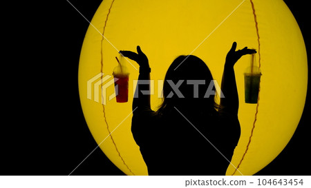 Young woman holding a glass of water in front of a yellow lantern resembling the moon 104643454