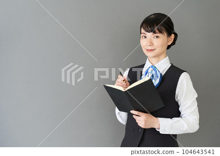 A receptionist and clerical woman wearing a ribbon-tie uniform and a vest for writing a notebook A receptionist and clerical woman wearing a ribbon-tie uniform and a vest for writing a notebook 104643541
