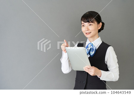 A woman in reception and clerical work wearing a ribbon tie uniform on a tablet operating vest A woman in reception and clerical work wearing a ribbon tie uniform on a tablet operating vest 104643549