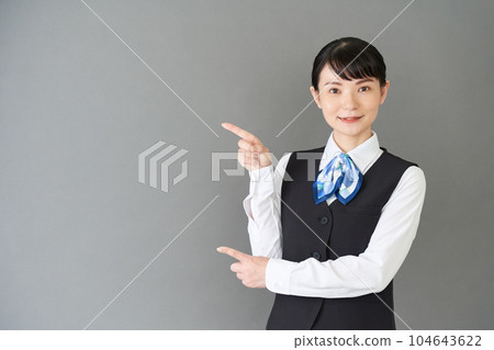 一位從事接待工作和文書工作的女性，穿著絲帶領帶制服，背心上用手指指著 104643622